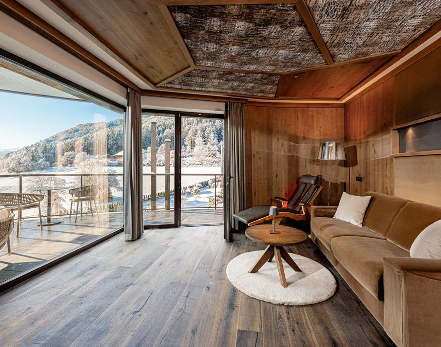 Wohnbereich einer Suite im Hotel Kronblick mit Holzverkleidung, Sofa und Balkon mit Winterpanorama